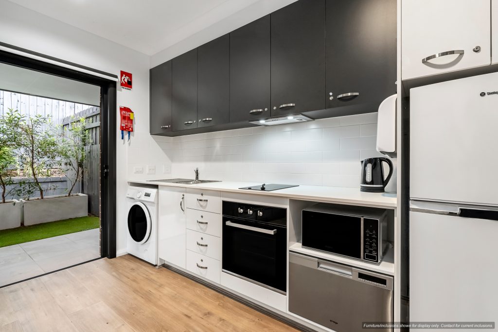 Modern kitchen in Concord, Inner West Sydney, featuring black and white cabinets, quality appliances—oven, microwave, refrigerator, washing machine—and a view of a small outdoor patio. 10E.