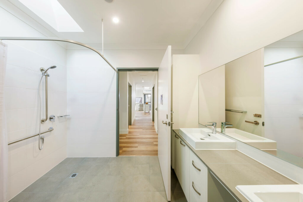 A spacious bathroom with a walk-in shower, double sink vanity, and a view into a hallway leading to other rooms in the serene Maroubra area of Sydney's Eastern Suburbs. The room has a clean and minimalistic design with neutral colors, providing an elegant retreat.