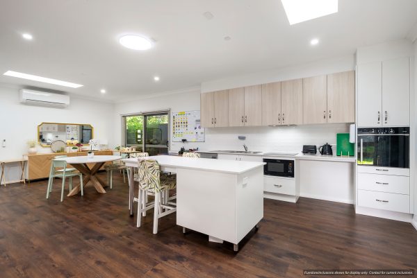 Modern kitchen and dining area in Narraweena, Northern Beaches, with white cabinets, wooden flooring, central island, dining table, appliances, and large windows allowing natural light.