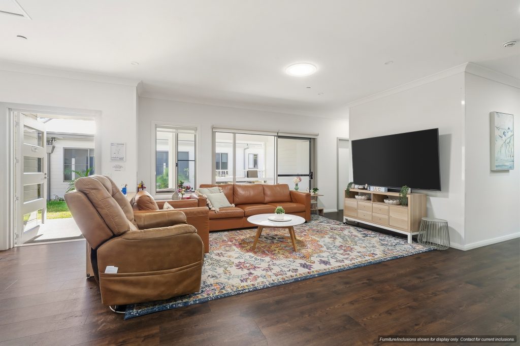 Modern living room in Narraweena, Sydney, with brown leather couches, a large area rug, flat-screen TV on a wooden console, and ample natural light from windows and an open door—perfect for enjoying the relaxed Northern Beaches lifestyle.