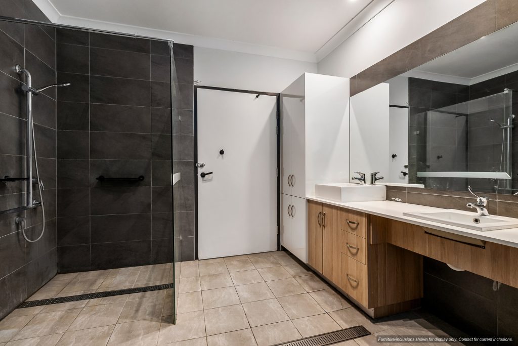 Modern bathroom in Concord featuring a walk-in shower, large mirror, white sink, wooden cabinetry, and tiled floors and walls—perfect for stylish Inner West Sydney living.