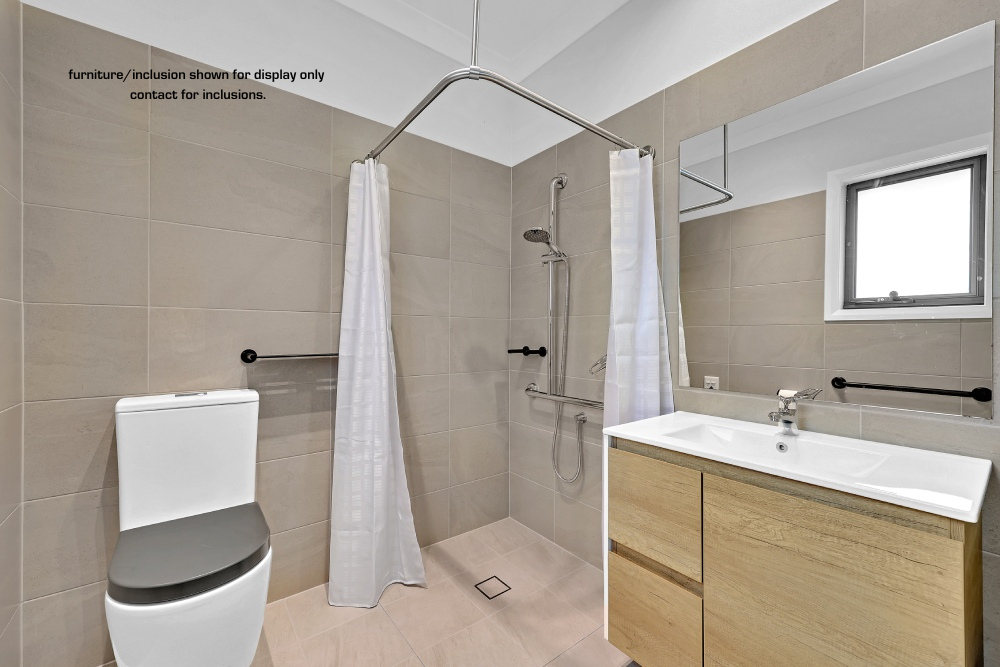 Accessible bathroom in 10F, Concord, Inner West Sydney, featuring a walk-in shower, grab bars, shower curtain, toilet, sink with wooden cabinet, and a mirror above the vanity.