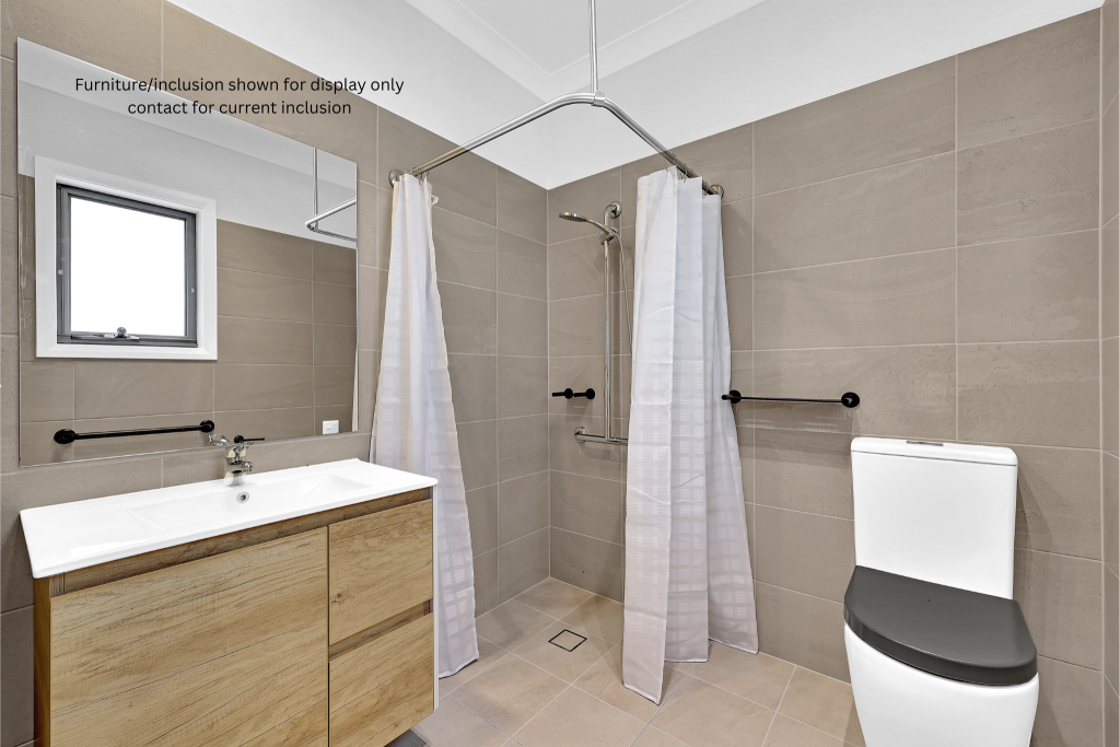 Modern accessible bathroom in Concord, Inner West Sydney, featuring beige tiles, a shower area with grab bars and curtains, a white toilet, and a wooden vanity with a sink and mirror.