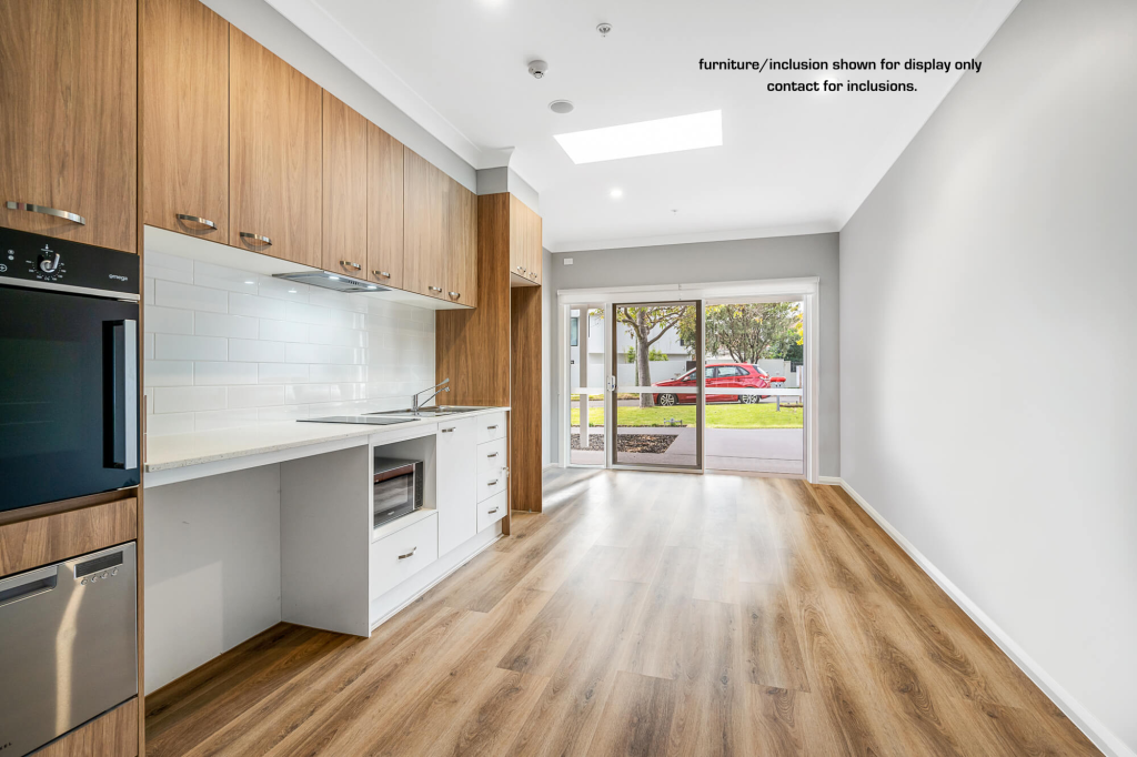 Modern, unfurnished kitchen and living area in Pagewood with wooden cabinets, built-in oven, white backsplash, large window, and sliding glass door leading outside. Located in Inner South Sydney 9B zone. Text on wall notes display inclusions.