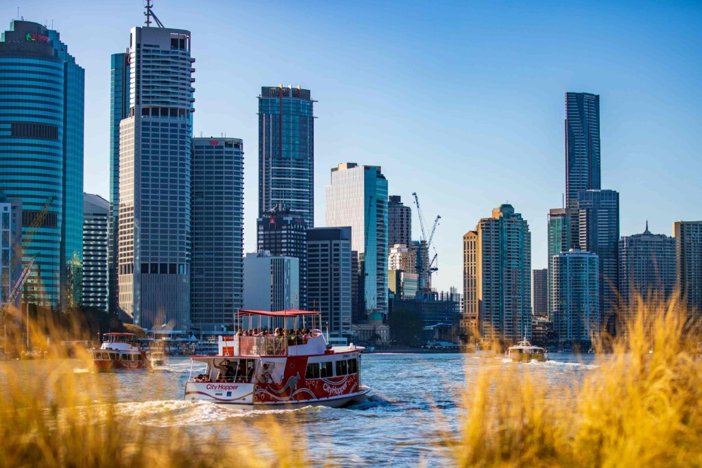 A boat is sailing down a river with tall buildings in the background.
