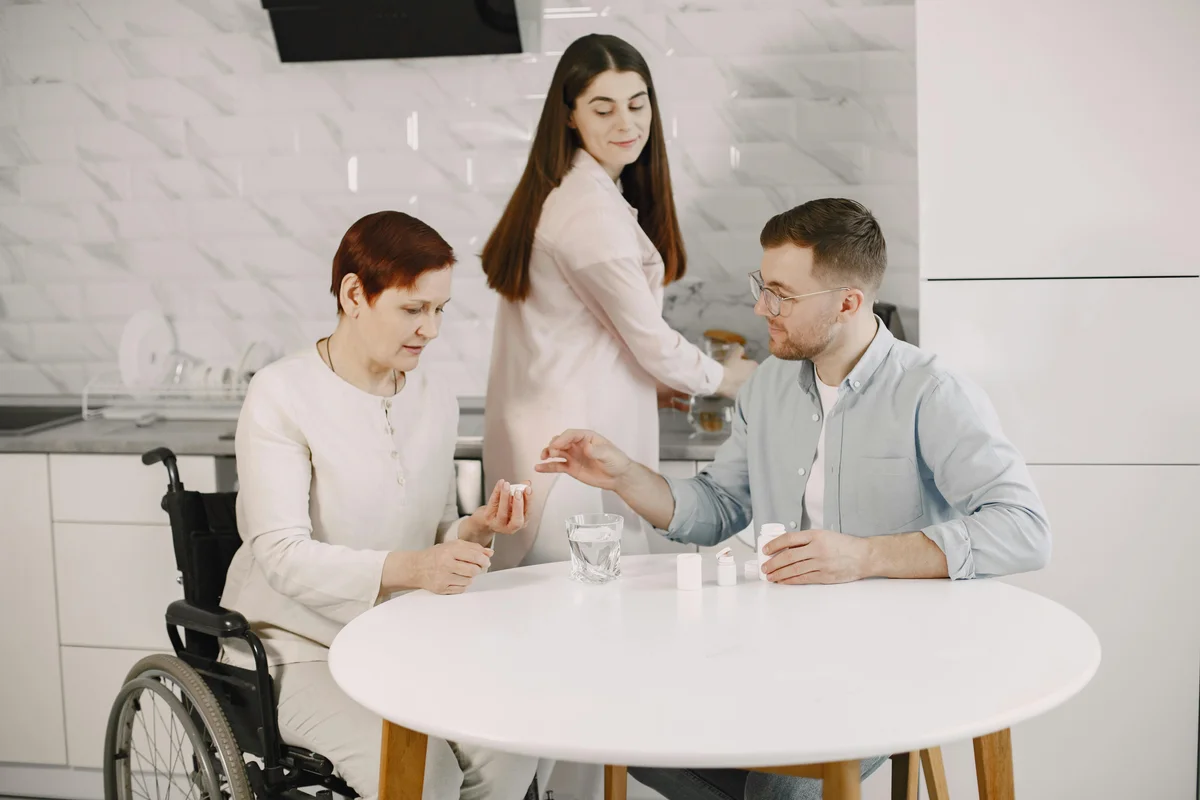 Support worker assisting person in wheelchair with medication in modern kitchen