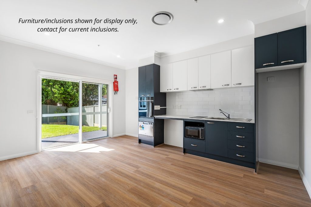 Modern kitchen with blue and white cabinets, built-in appliances, and wood flooring; sliding glass doors open to a fenced backyard in Sydney’s Sutherland Shire. Text notes display-only furniture and inclusions.