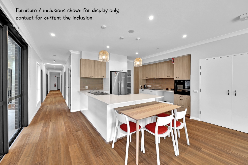 Modern kitchen with a central island, built-in appliances, and wooden cabinets. A dining table with white chairs is positioned next to the island, highlighting sleek living in Parramatta. Caption mentions furniture is for display only.