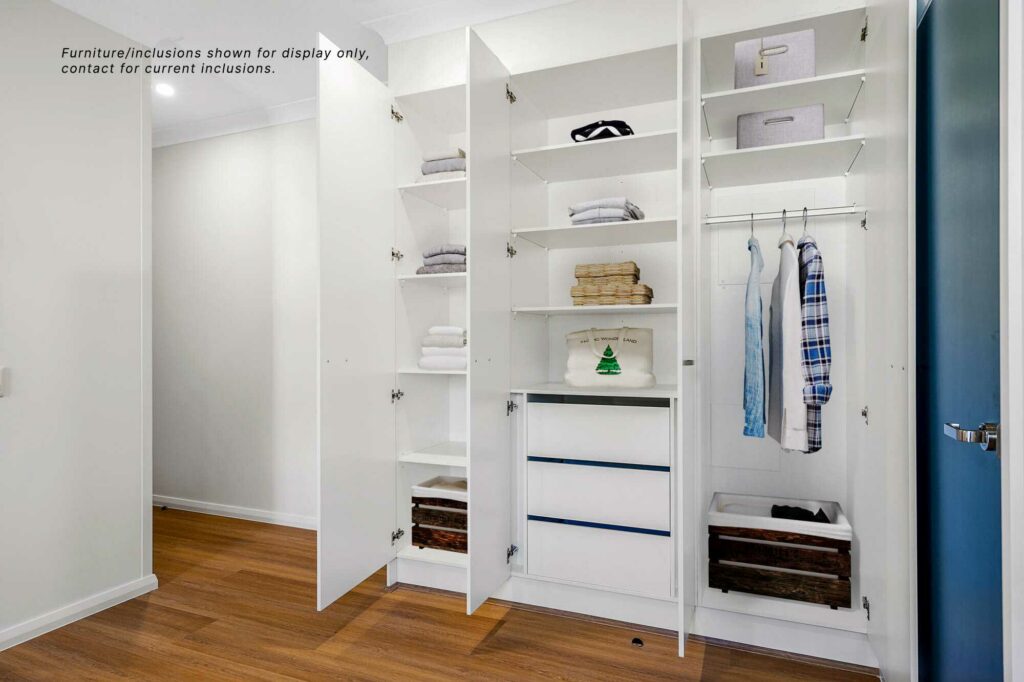 Open white wardrobe with multiple shelves, drawers, and hanging space containing folded towels, clothes, and boxes. Note on the upper left says, "Furniture/inclusions shown for display only. Contact for current inclusions." Perfect for a stylish home in Central Coast NSW.