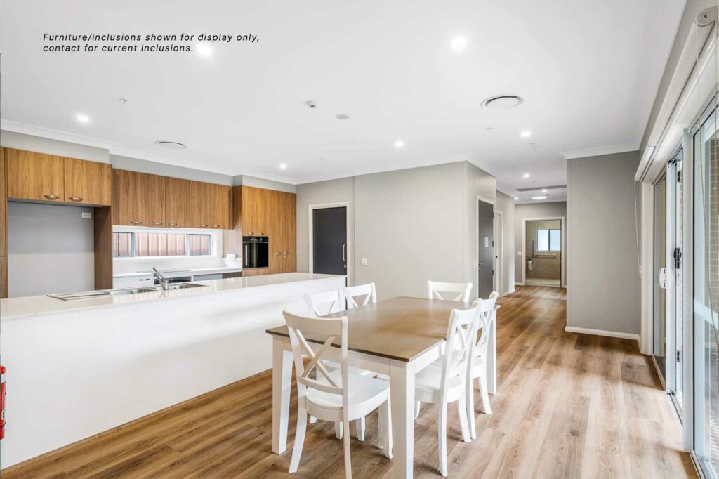 Modern open-concept kitchen and dining area in Pagewood with wooden flooring, white cabinets and countertops, and a wooden dining table with white chairs. Note: Furniture shown is for display only.