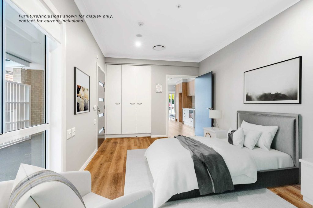 Modern bedroom in Pagewood, Inner South Sydney, featuring a double bed, armchair, built-in wardrobe, wall art, and wooden flooring—adjacent to an open doorway leading to a stylish kitchen at 9C.