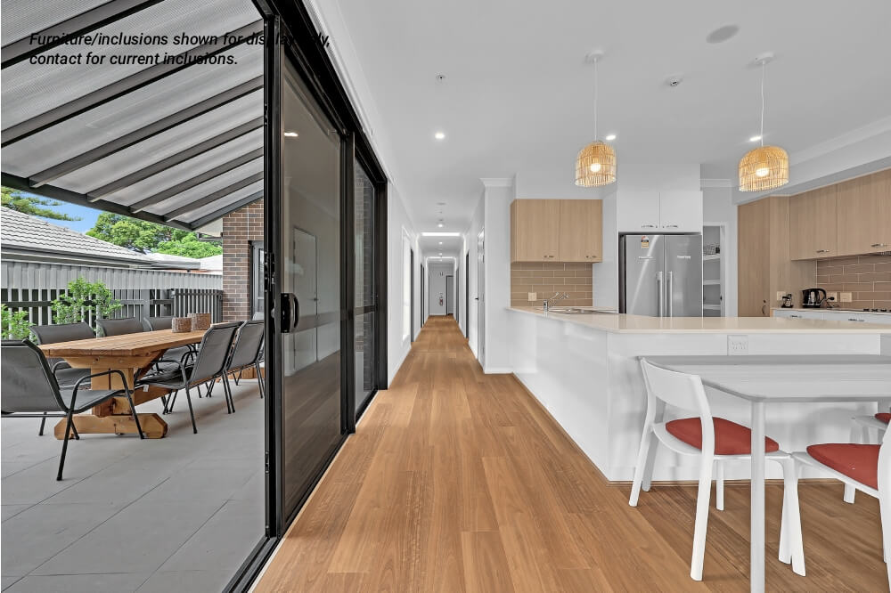 Modern open-plan kitchen and dining area in Concord, Inner West Sydney, with wooden flooring, white cabinets, pendant lights, and sliding glass doors opening to an outdoor patio with table and chairs.