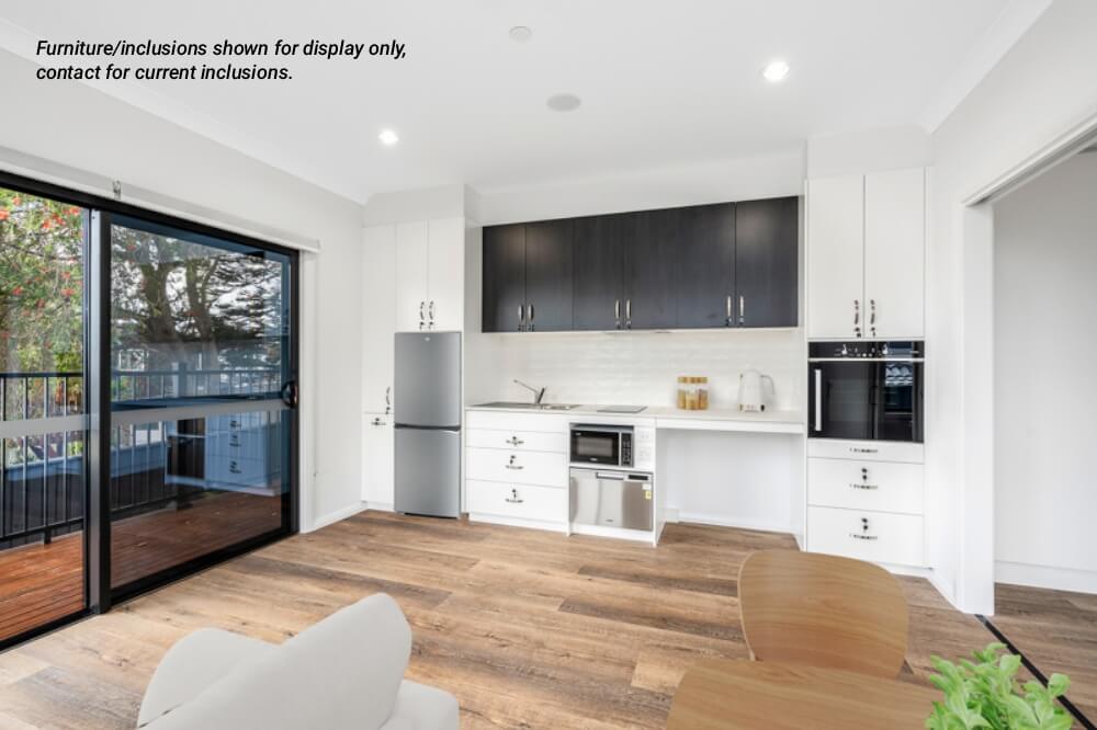 Modern kitchen with white cabinets, stainless steel appliances, light wood flooring, and glass sliding doors opening to a deck—enjoy stylish living in Sydney’s vibrant Northern Beaches. Furniture/inclusions shown are for display only.