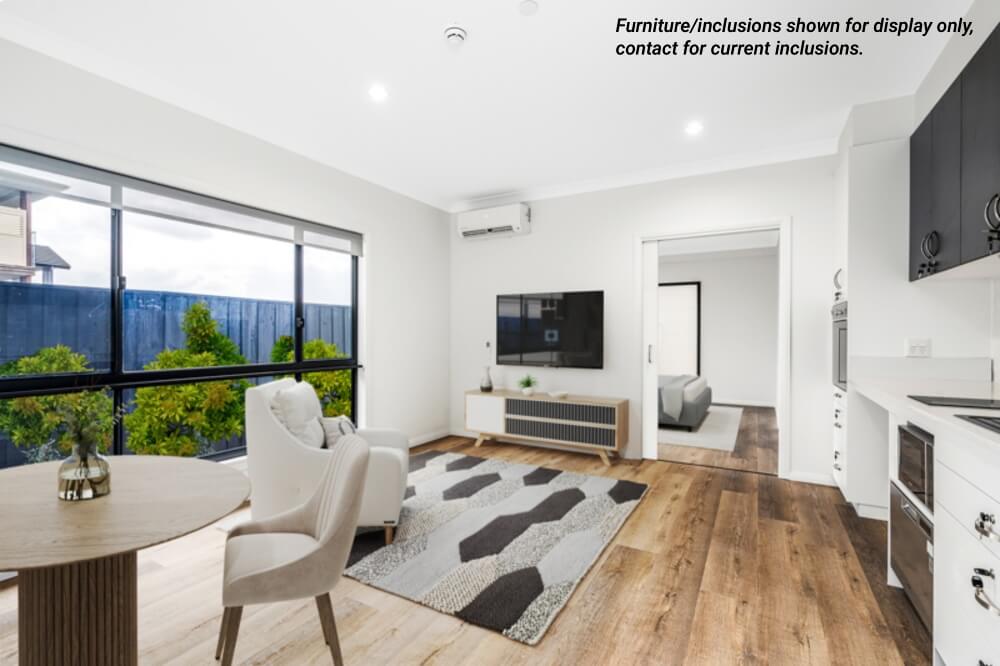 Modern living room in Narraweena with large window, TV mounted on wall, armchair, round dining table, open kitchen area, and wood flooring. Text note about furniture inclusions is visible in the image. Enjoy Northern Beaches lifestyle.