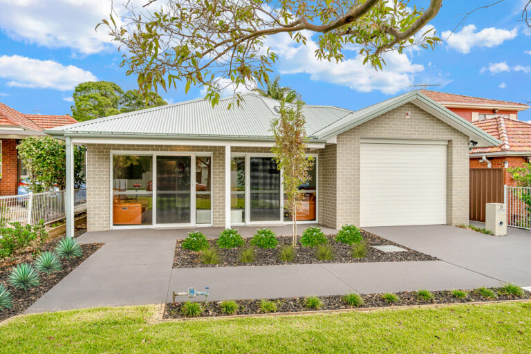 Modern single-story house in the desirable Inner South of Sydney with a manicured front yard, a covered porch, and a single-car garage. The exterior is light-colored with large windows and a neatly landscaped garden that enhances its charm.
