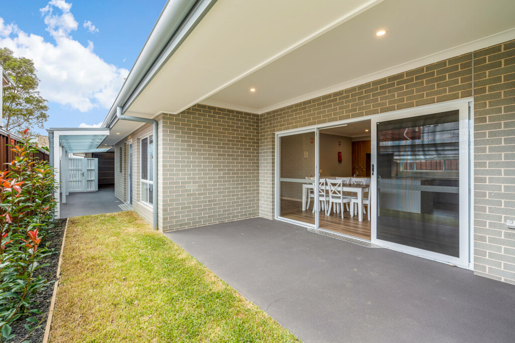A modern outdoor patio area in South Sydney features a covered section, sliding glass doors leading to an indoor dining area, brick walls, and a small landscaped garden on the side.