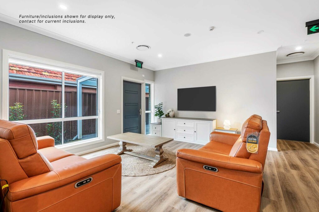 Living room with brown leather seating, wooden coffee table, TV mounted on the wall, white sideboard, and large window. Note on wall mentions furniture/inclusions are for display only. Located in the vibrant suburb of Pagewood in Inner South Sydney.