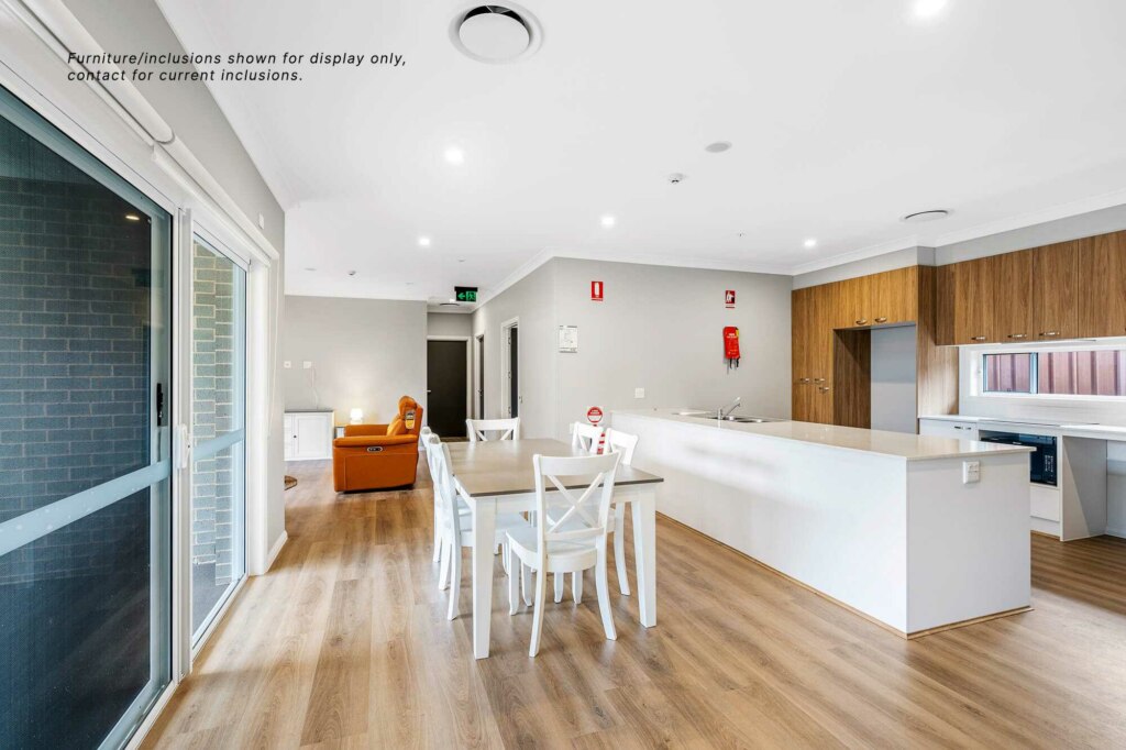 Modern kitchen and dining area with white countertops, wooden cabinetry, a dining table with chairs, and a lounge area with an orange sofa in the heart of Pagewood. Note about furniture display; contact for current inclusions. Ideal for those seeking vibrant inner South Sydney living.