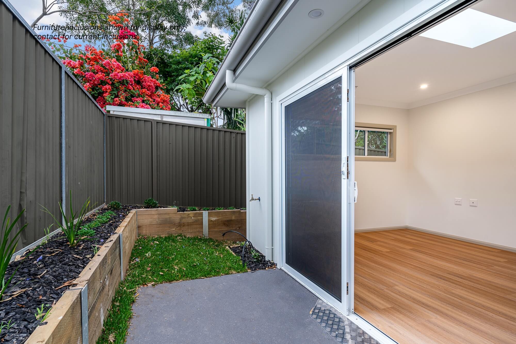 Nestled at 8A Pendle Hill, this small backyard boasts a charming garden bed and a paved area, perfectly complementing the modern room with its sleek wooden flooring and inviting sliding glass door.