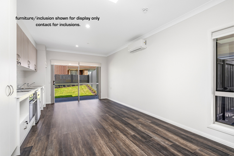 Unfurnished modern open-plan living area in Narraweena, Northern Beaches, featuring kitchenette, wood-look flooring, white walls, sliding glass door to backyard, and large window. Text overlay notes display-only inclusions.