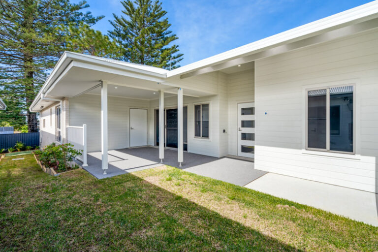Single-story modern house in Narraweena with beige siding, a covered front porch, and a small lawn. Large windows and a simple entrance are visible. Located in Sydney's Northern Beaches area, this home offers a blend of contemporary design and coastal charm.