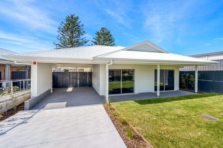 Front view of a modern single-story house with a white façade, a spacious driveway, and a well-maintained lawn under a clear blue sky in the serene suburb of Narraweena, Northern Beaches.