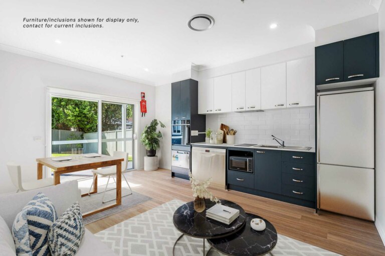 Modern kitchen and dining area with black and white cabinetry, stainless steel appliances, wood flooring, and a sliding glass door leading to a small outdoor area. Located at 30B in Sutherland, NSW.